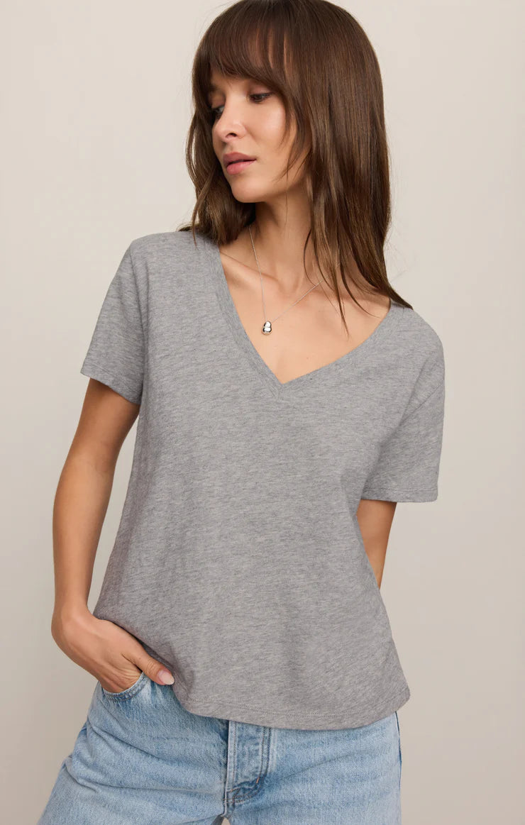 Woman wearing a gray V-neck t-shirt and blue jeans against a beige background