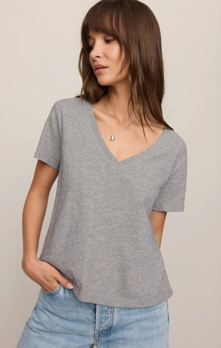 Woman wearing a gray V-neck t-shirt and blue jeans against a beige background