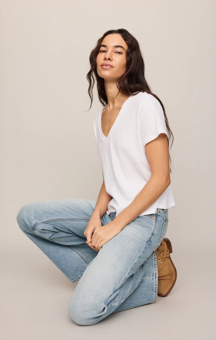 Woman wearing a white top and blue jeans sitting on the floor against a plain background