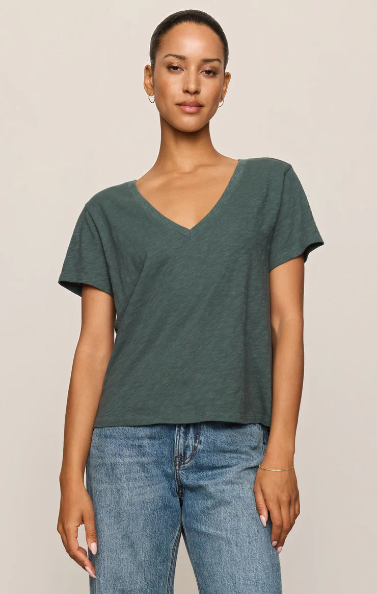 Woman wearing a green t-shirt and blue jeans against a beige background