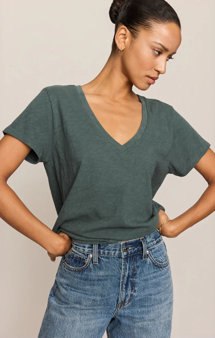Woman wearing a green t-shirt and blue jeans against a plain background