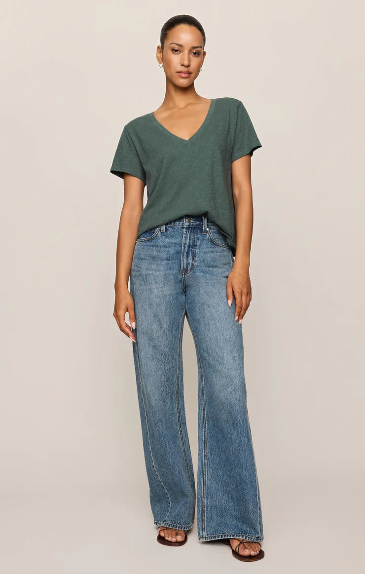 Woman wearing a green t-shirt and blue jeans on a beige background