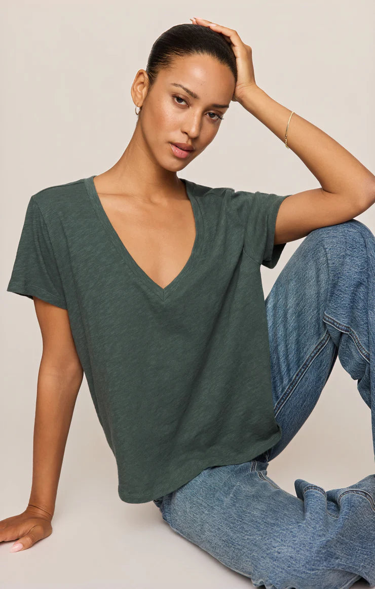Woman wearing a green t-shirt and blue jeans sitting on the floor against a plain background