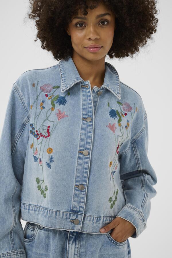 Woman wearing a denim jacket with floral embroidery on a white background