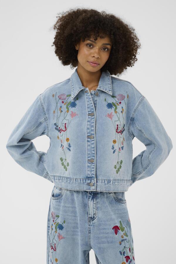 Woman wearing a light blue denim jacket with floral embroidery on a white background