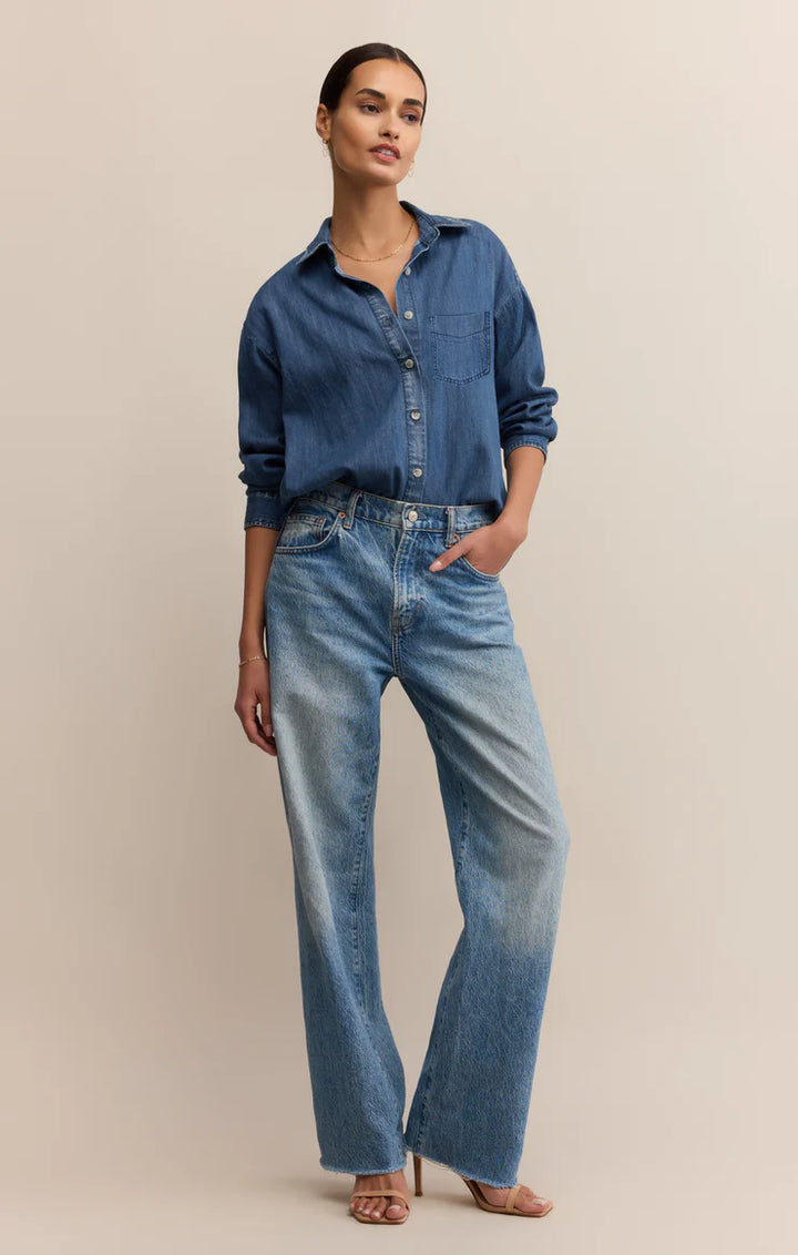 Woman wearing a blue denim shirt and jeans on a beige background