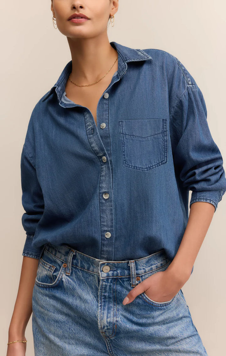 Person wearing a blue denim shirt and jeans against a beige background