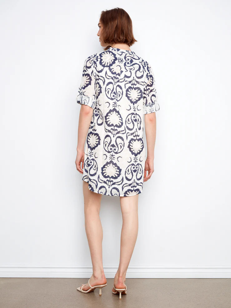 Woman wearing a white dress with black pattern against a plain background