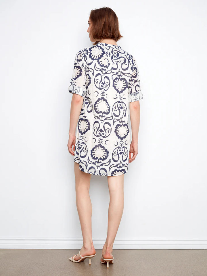 Woman wearing a white dress with black pattern against a plain background