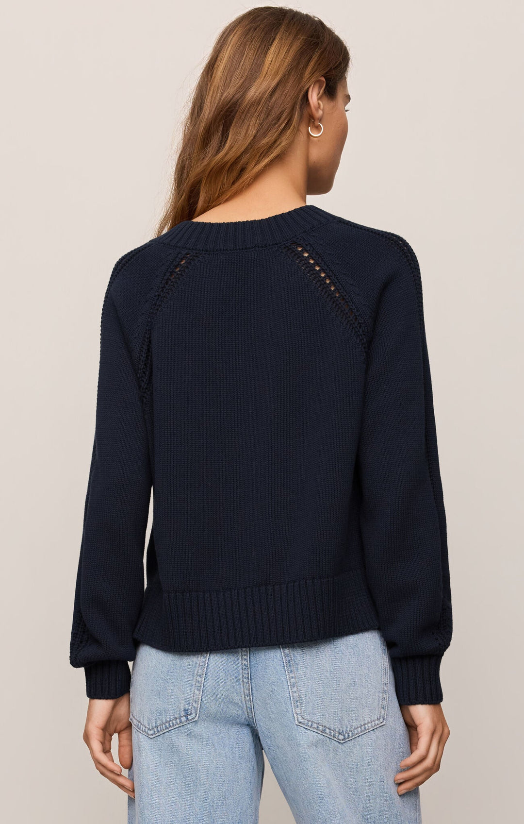 Person wearing a navy sweater with decorative buttons on a plain background