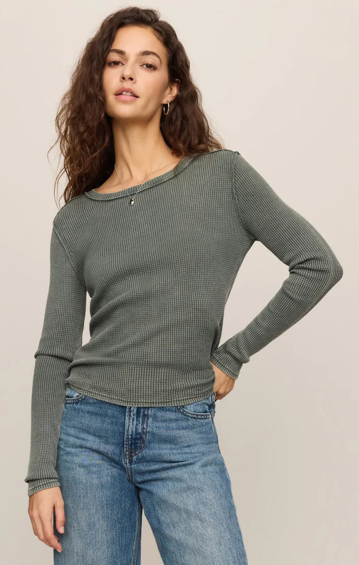 Woman wearing a green long-sleeve top and blue jeans against a plain background
