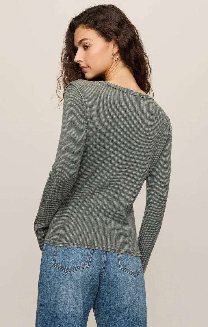 Woman wearing a green ribbed sweater and blue jeans on a beige background