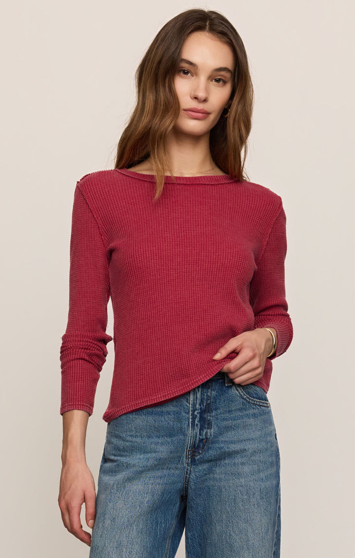 A woman wearing a ribbed long-sleeve knit sweater in a dusty rose pink color, paired with blue jeans, against a solid light beige background.