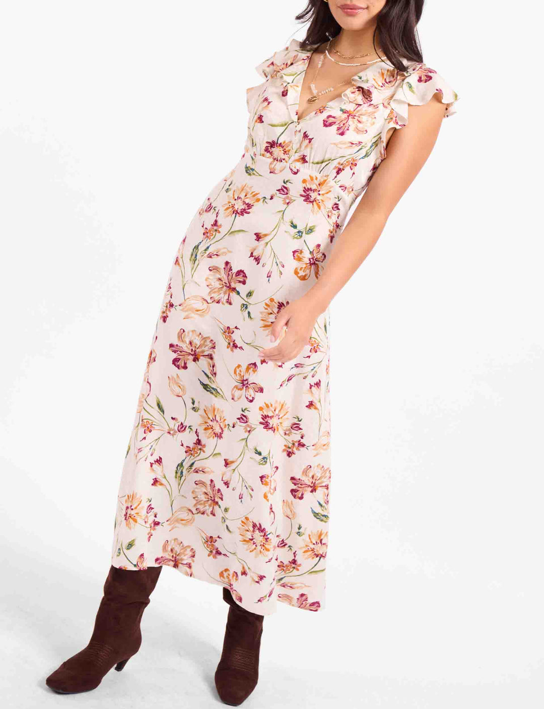 A woman models a floral midi dress with ruffled cap sleeves and brown heeled ankle boots against a plain white studio background.