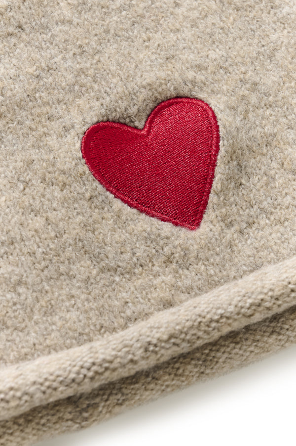Close-up of a beige knit fabric item featuring an embroidered red heart on the front.
