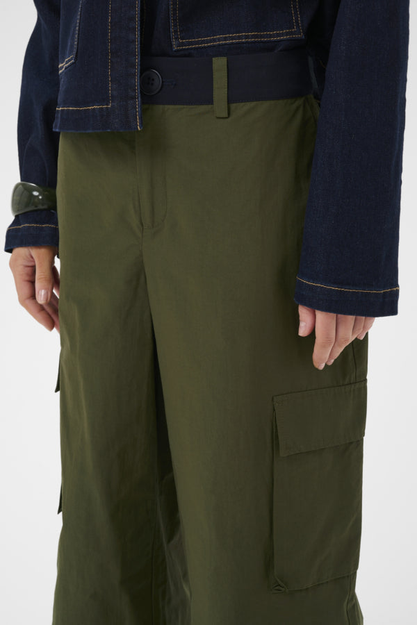 Olive green wide-leg cargo pants with a large flap pocket on the right leg, shown on a model wearing a dark navy jacket against a plain white background.