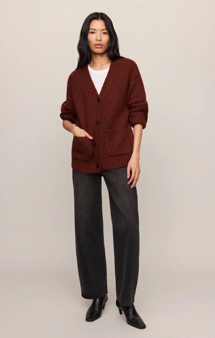 Woman wearing a brown cardigan, white shirt, gray pants, and black shoes on a beige background