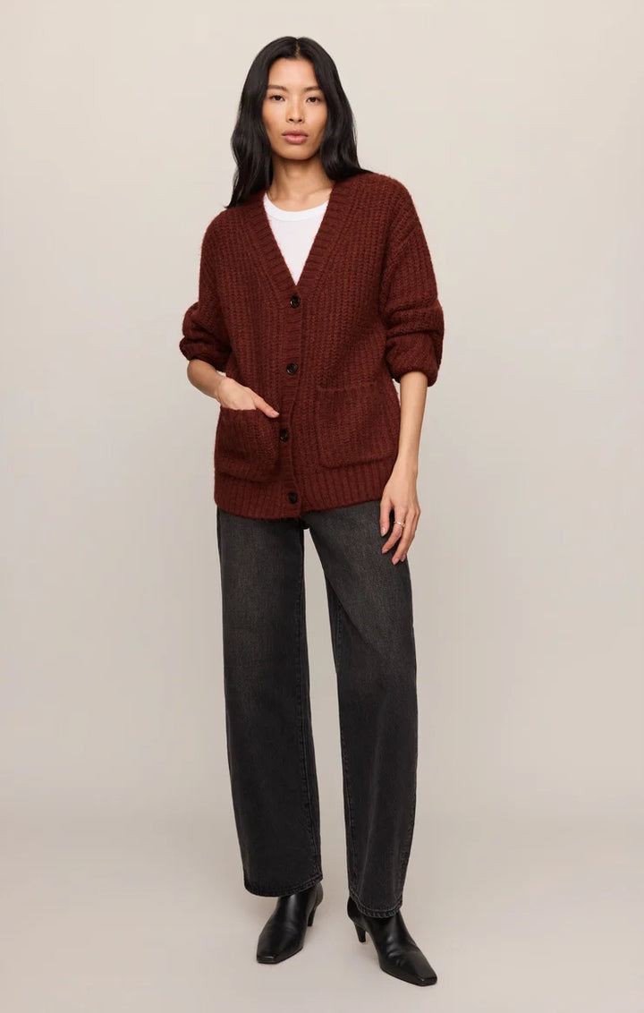 Woman wearing a brown cardigan, white shirt, gray pants, and black shoes on a beige background