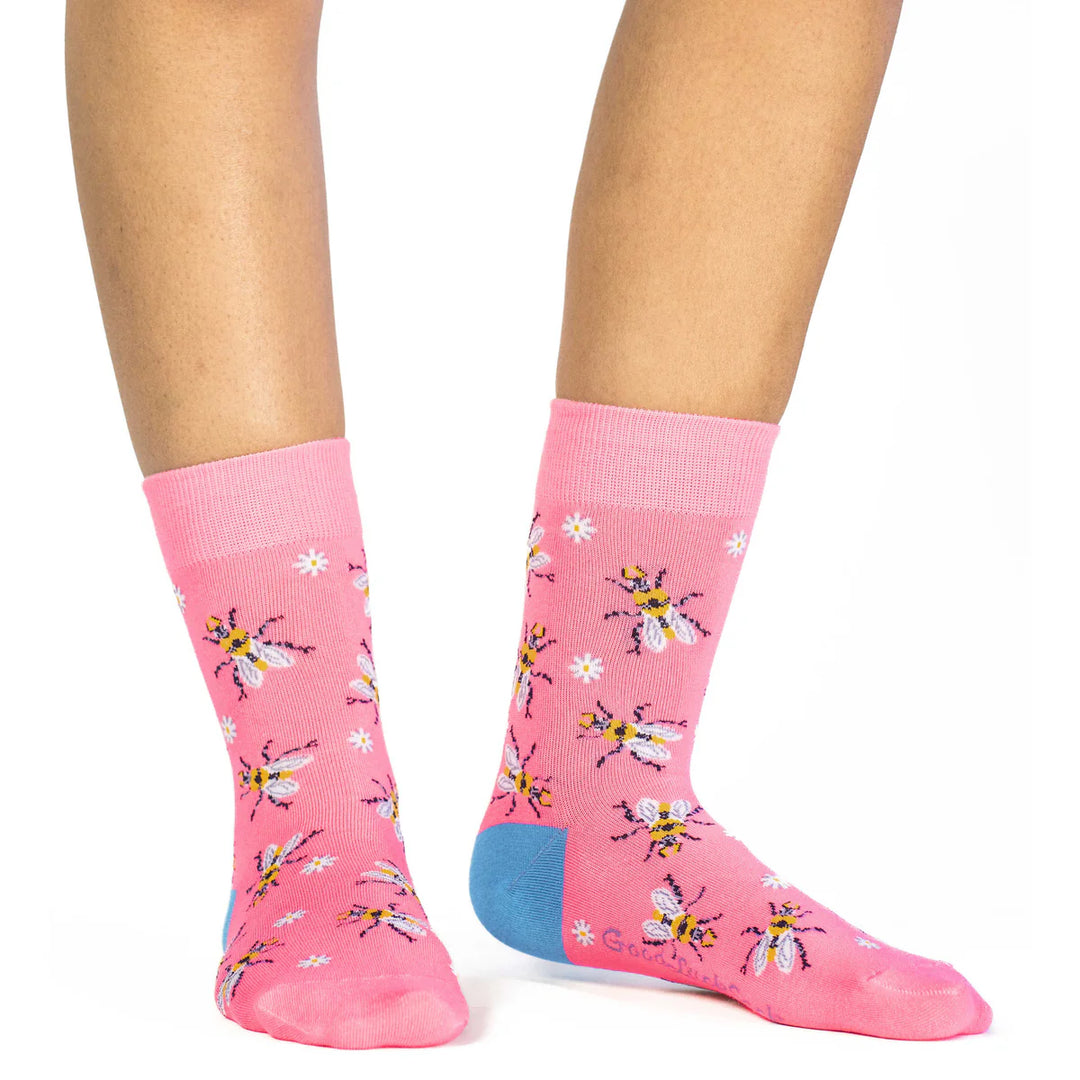A pair of pink crew socks with a pattern of yellow and purple bees and white daisies, worn on a person&