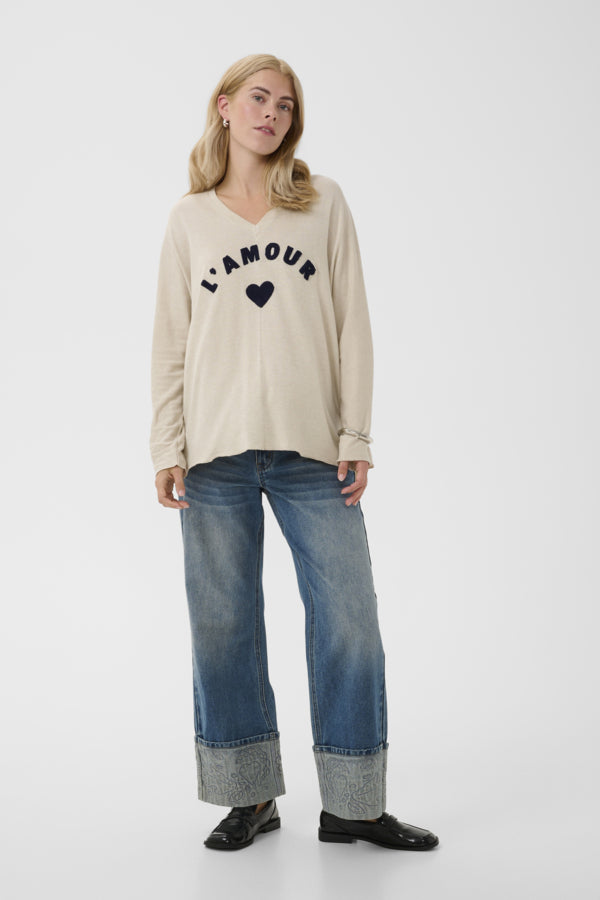 A woman modeling a beige long-sleeve V-neck sweater with &