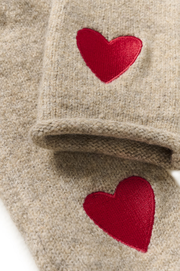 Close-up of a beige knit garment with two red heart appliqués on the cuff and body.