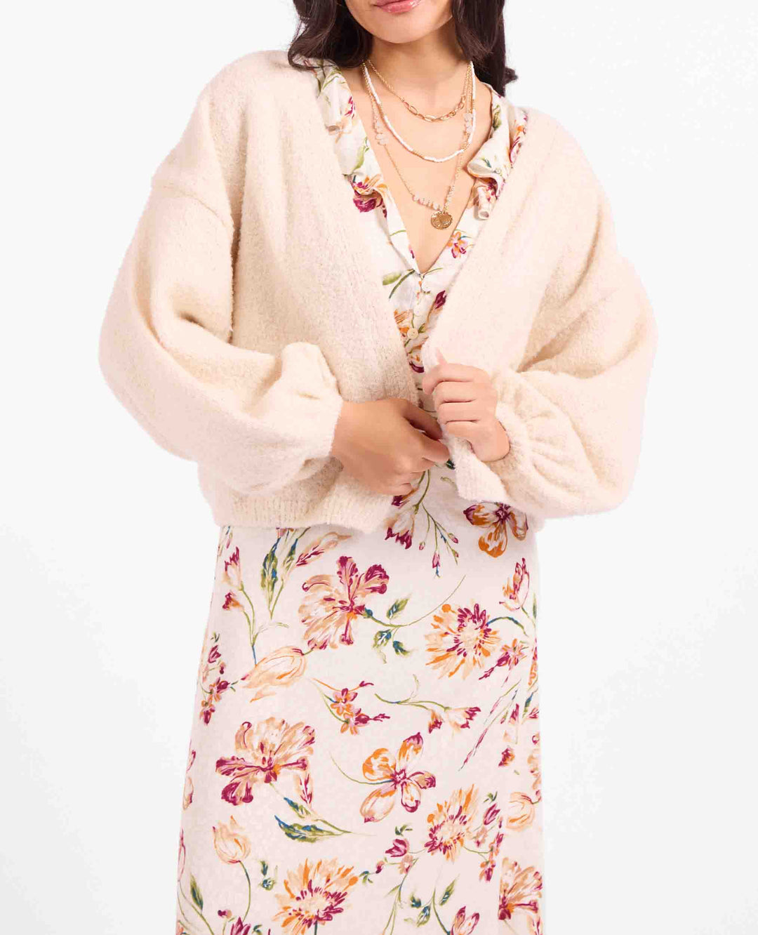 A woman wearing a cream fuzzy cropped cardigan over a floral print dress, photographed against a plain white background.