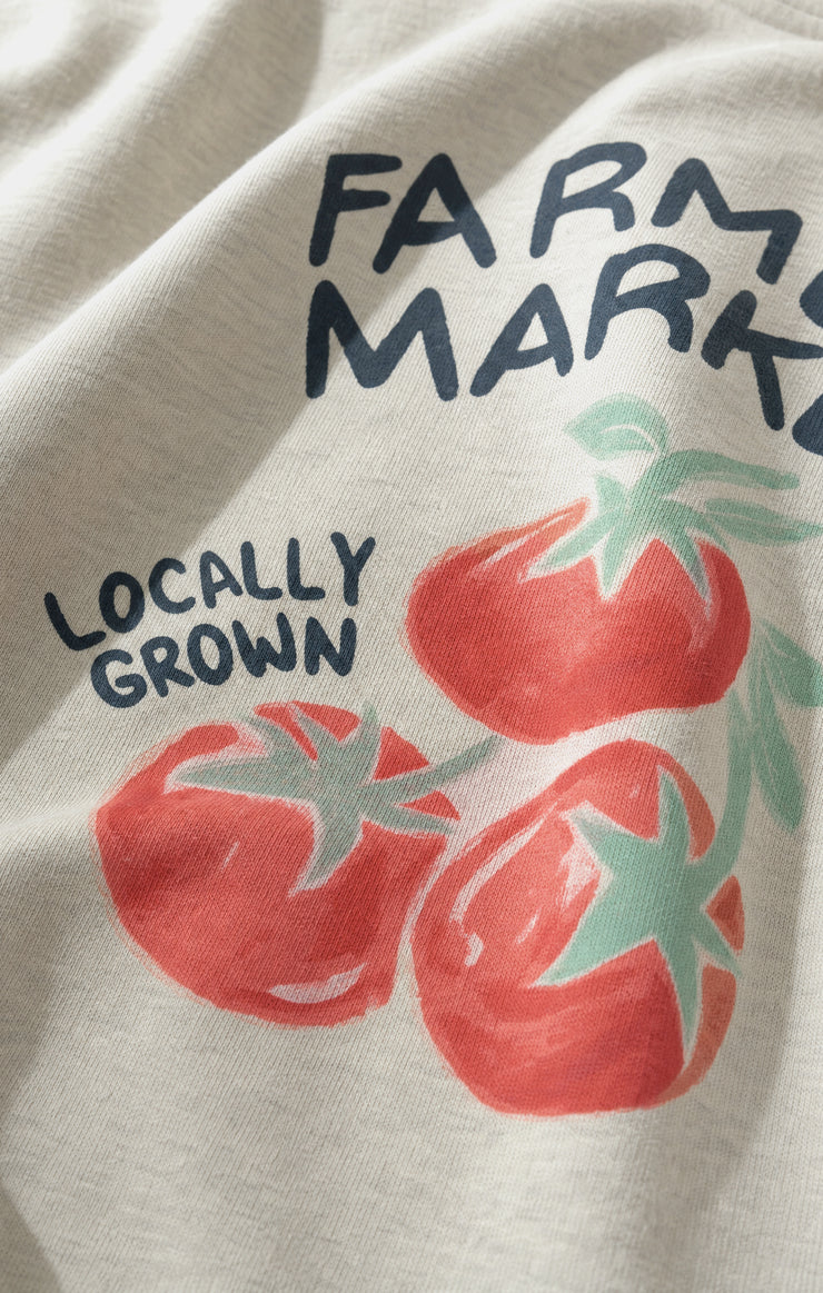 Close-up of a light heather gray fabric garment featuring a printed graphic of three red tomatoes with green stems and the text &