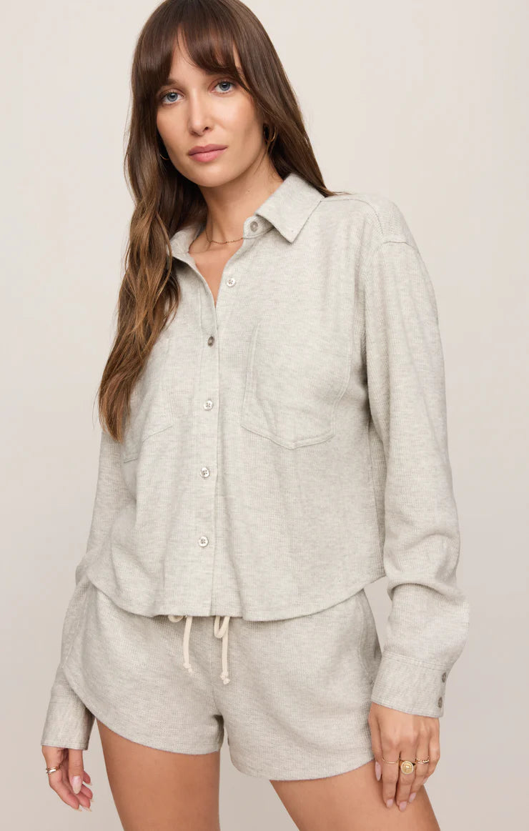Woman wearing a light gray button-up shirt and shorts set against a plain background