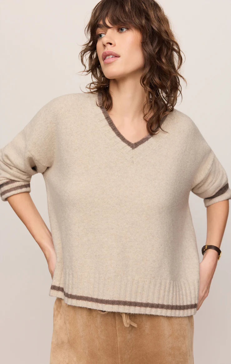 Woman wearing a beige sweater with brown trim against a plain background