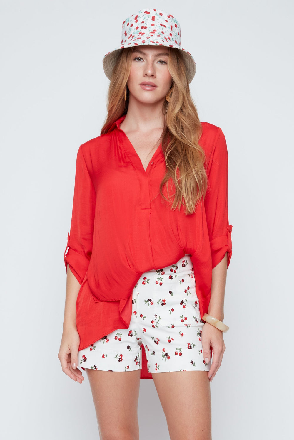 Woman wearing a red blouse, white shorts with red patterns, and a patterned hat on a white background