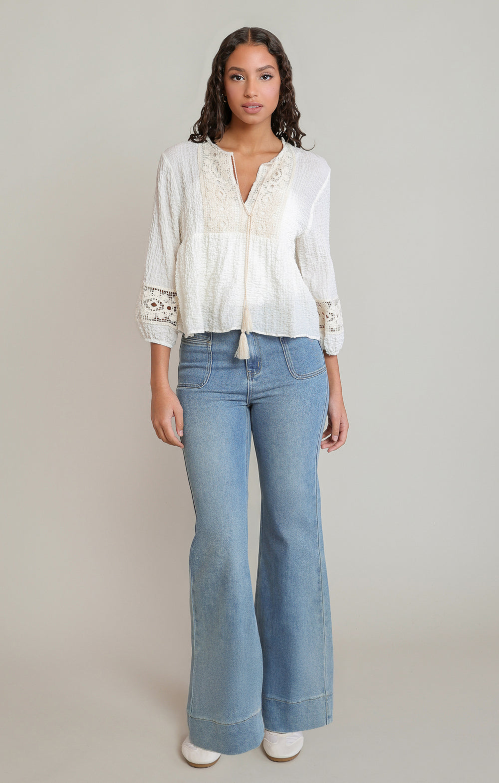 Woman wearing a white blouse with lace details and light blue jeans on a plain background