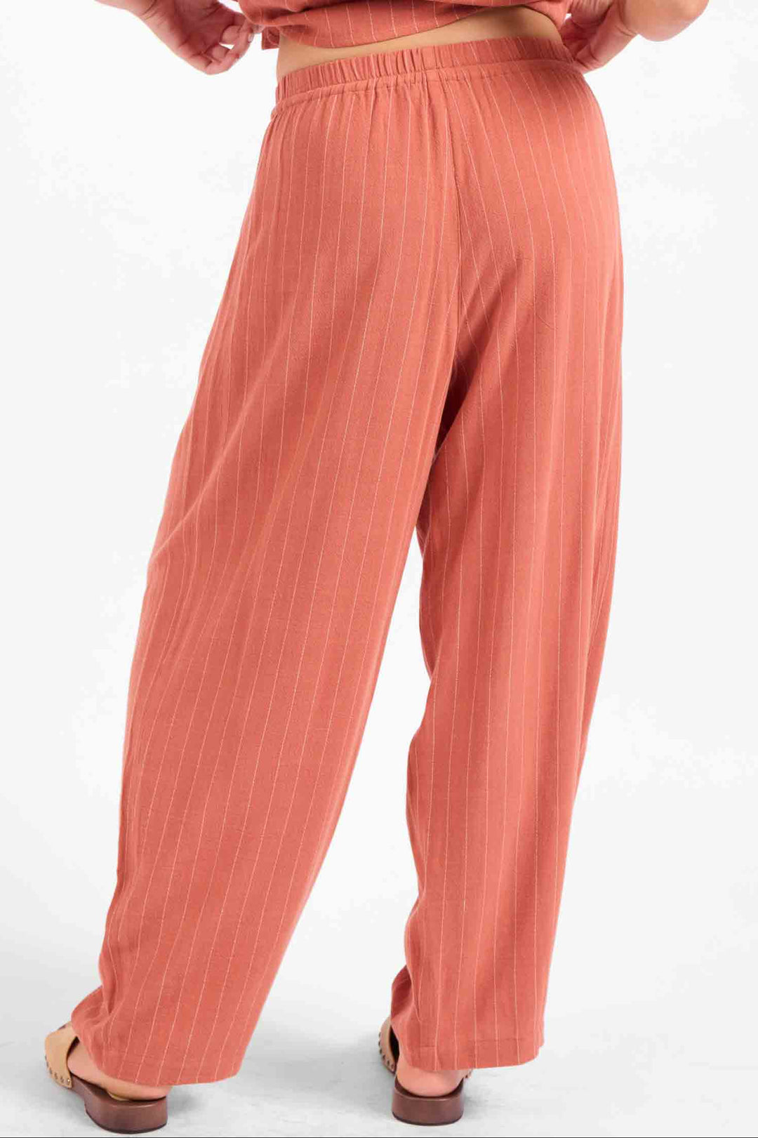 A person shown from the back wearing loose, wide-leg peach-pink pants with a matching top, photographed against a plain light background.