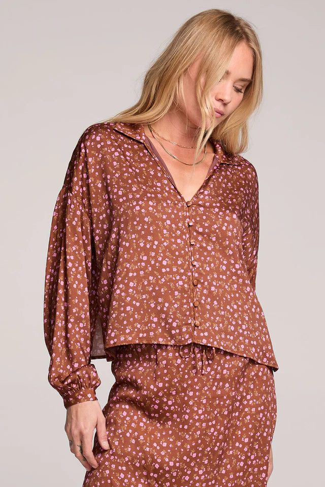 Woman wearing a brown floral blouse and skirt set against a plain background