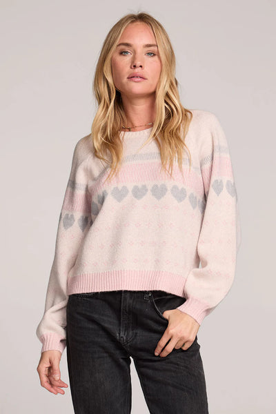 Woman wearing a light pink sweater with heart patterns on a plain background