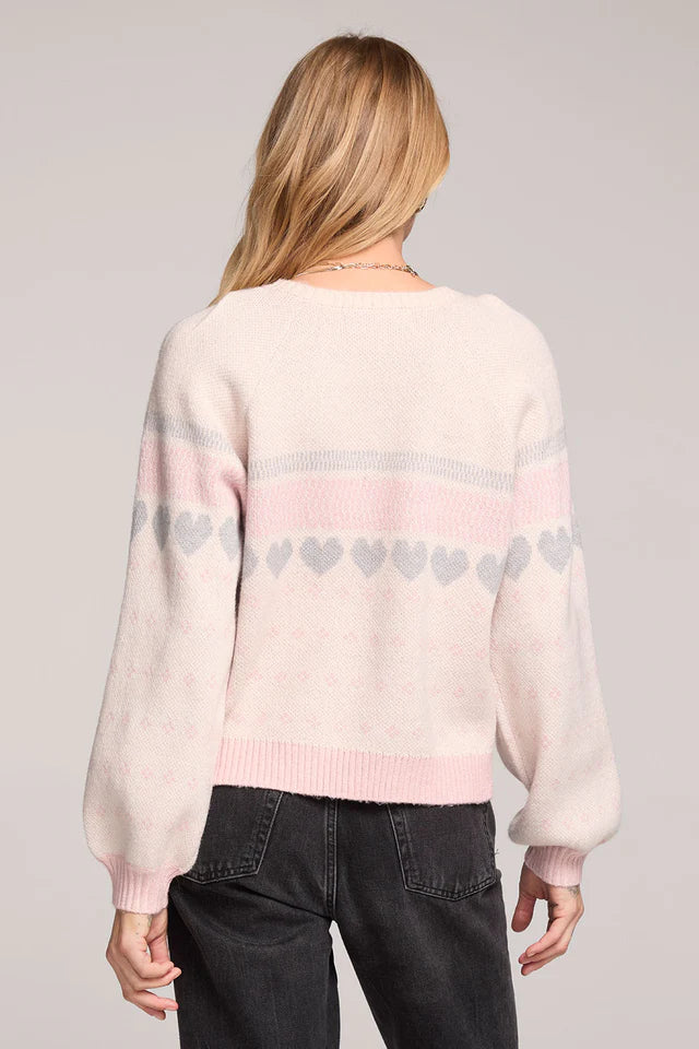 Person wearing a light pink sweater with heart patterns on a plain background