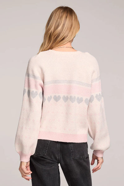 Person wearing a light pink sweater with heart patterns on a plain background