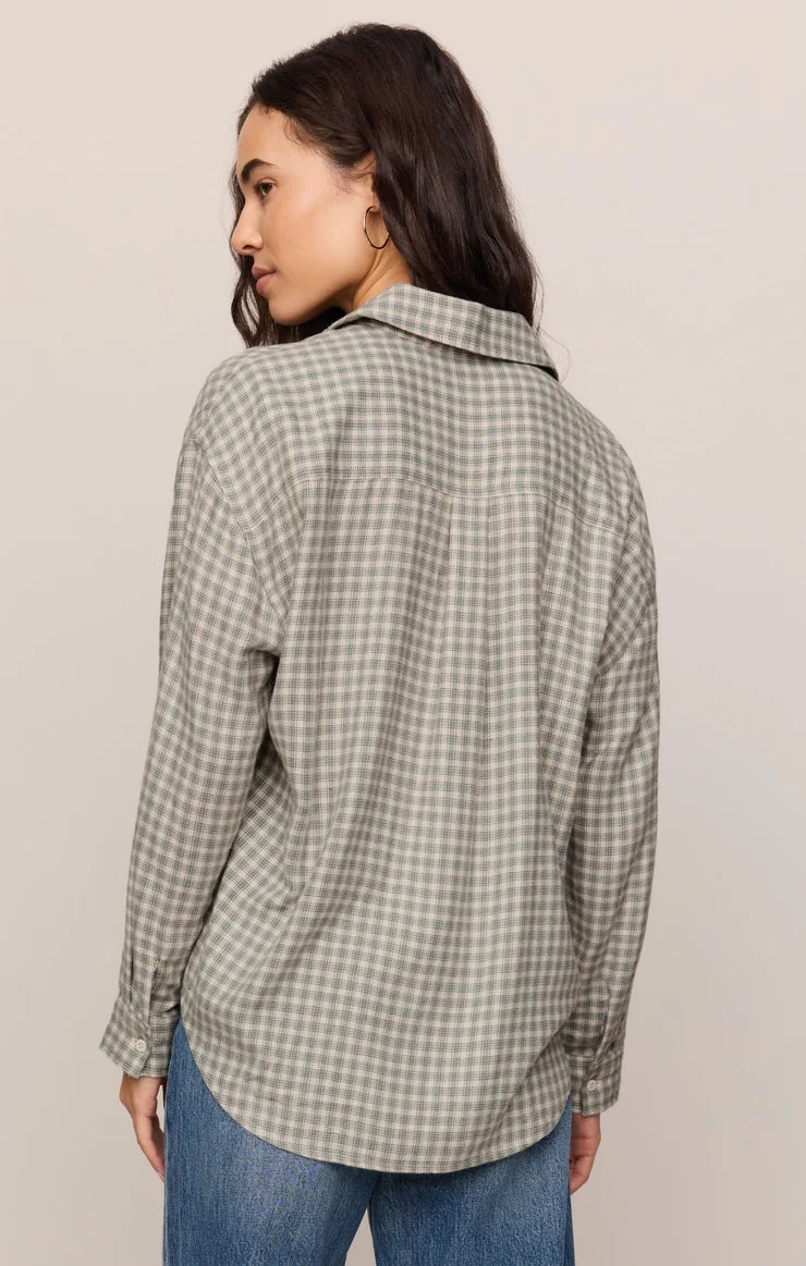 A woman shown from the back wearing a long-sleeve button-up shirt with a small-scale green and white gingham pattern, paired with blue jeans, against a plain light beige background.