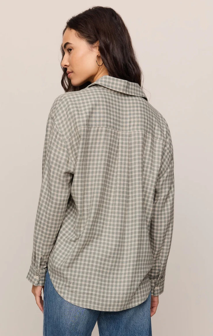 A woman shown from the back wearing a long-sleeve button-up shirt with a small-scale green and white gingham pattern, paired with blue jeans, against a plain light beige background.