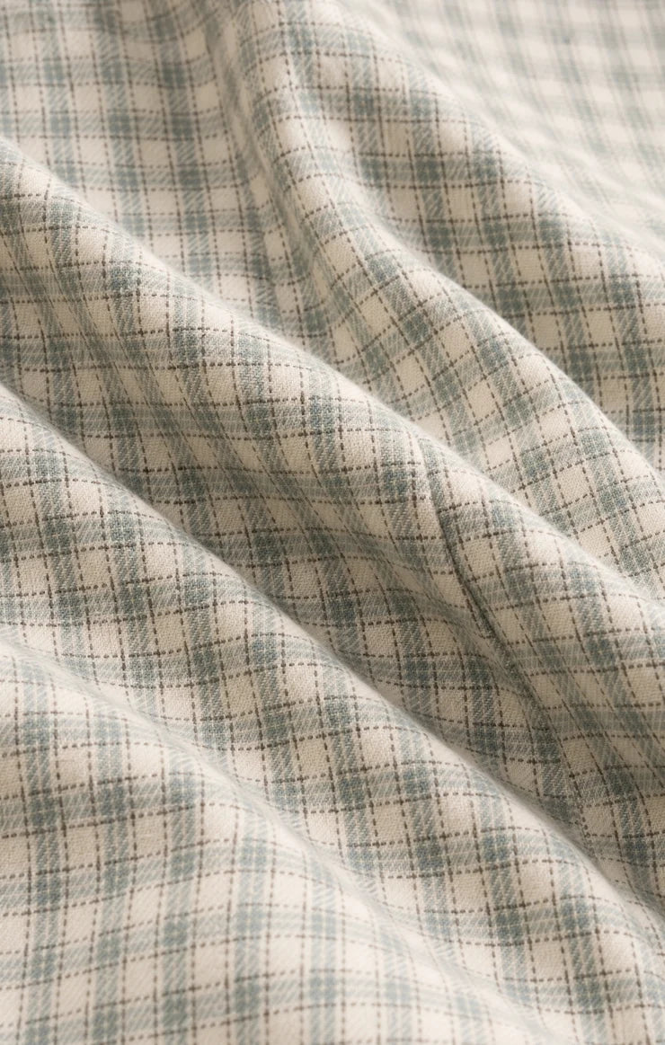 A close-up of draped fabric with a soft plaid pattern in muted sage green and cream.