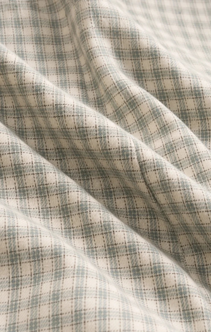 A close-up of draped fabric with a soft plaid pattern in muted sage green and cream.