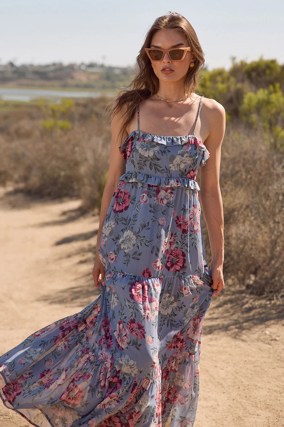 Woman in a floral dress standing on a dirt path with a scenic background