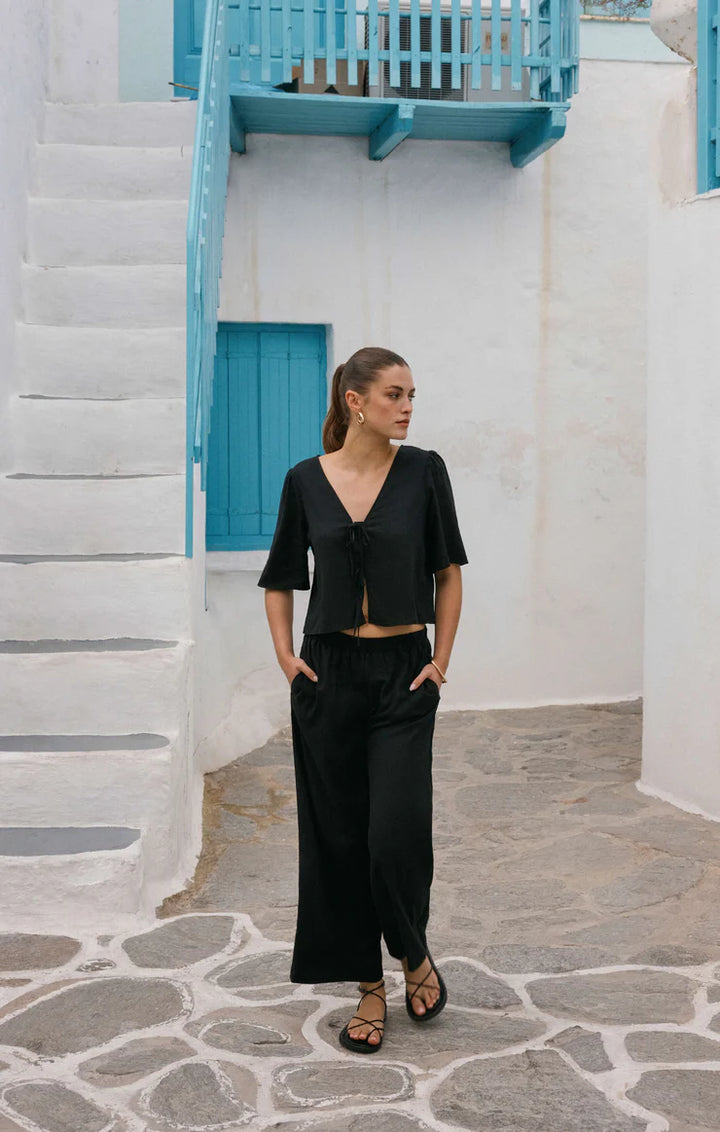 Woman in a black outfit standing in a narrow alley with white walls and blue accents.