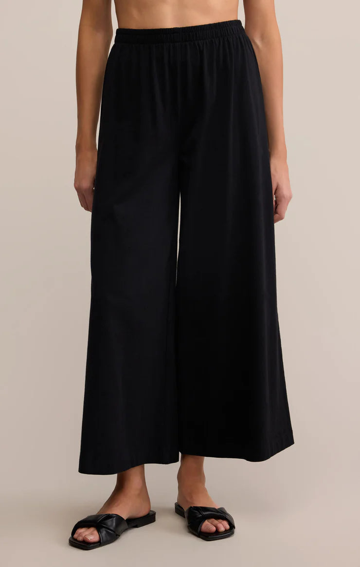 Person wearing black wide-leg pants on a beige background