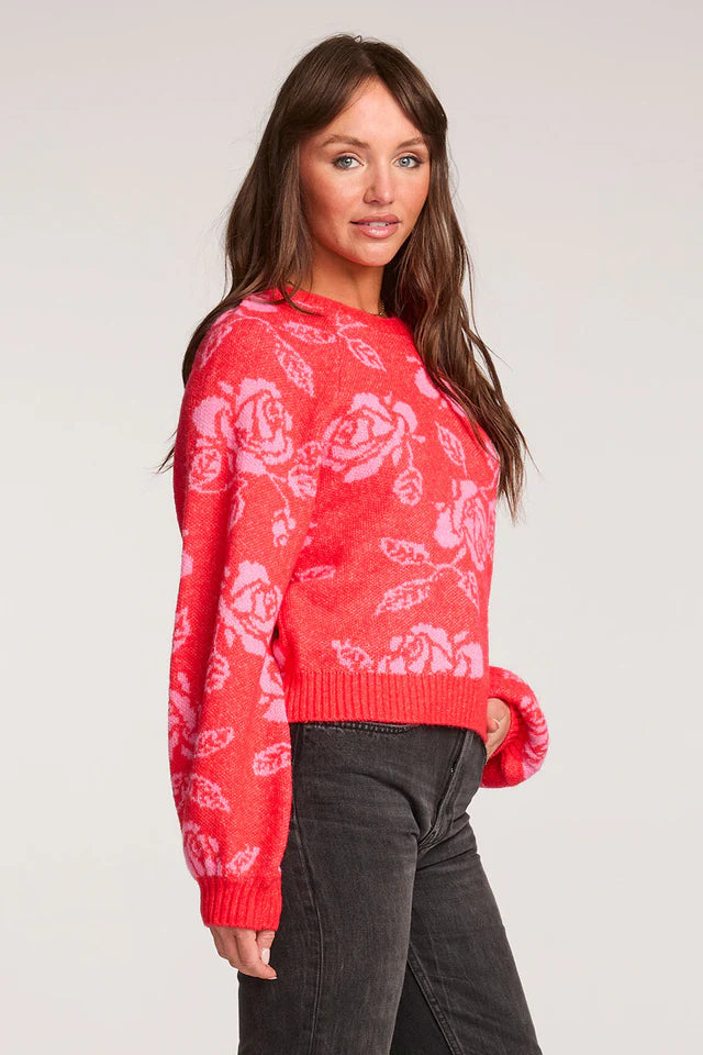 Woman wearing a red sweater with white floral patterns on a plain background