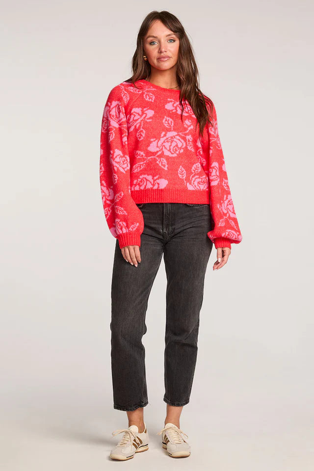 Woman wearing a red floral sweater and black jeans on a white background