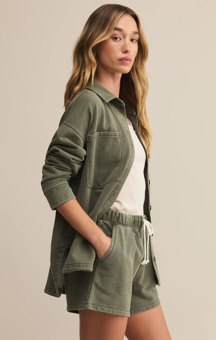 Woman wearing an olive green jacket and shorts on a beige background