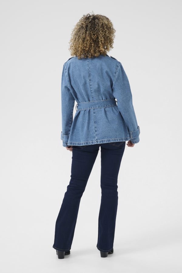 Person wearing a blue denim jacket and dark jeans on a white background