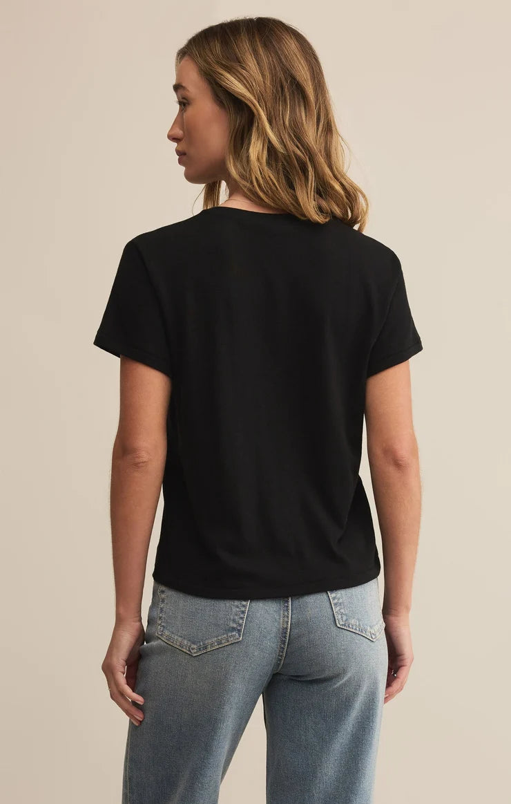 Woman wearing a black t-shirt and blue jeans against a beige background