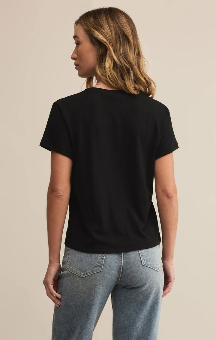 Woman wearing a black t-shirt and blue jeans against a beige background