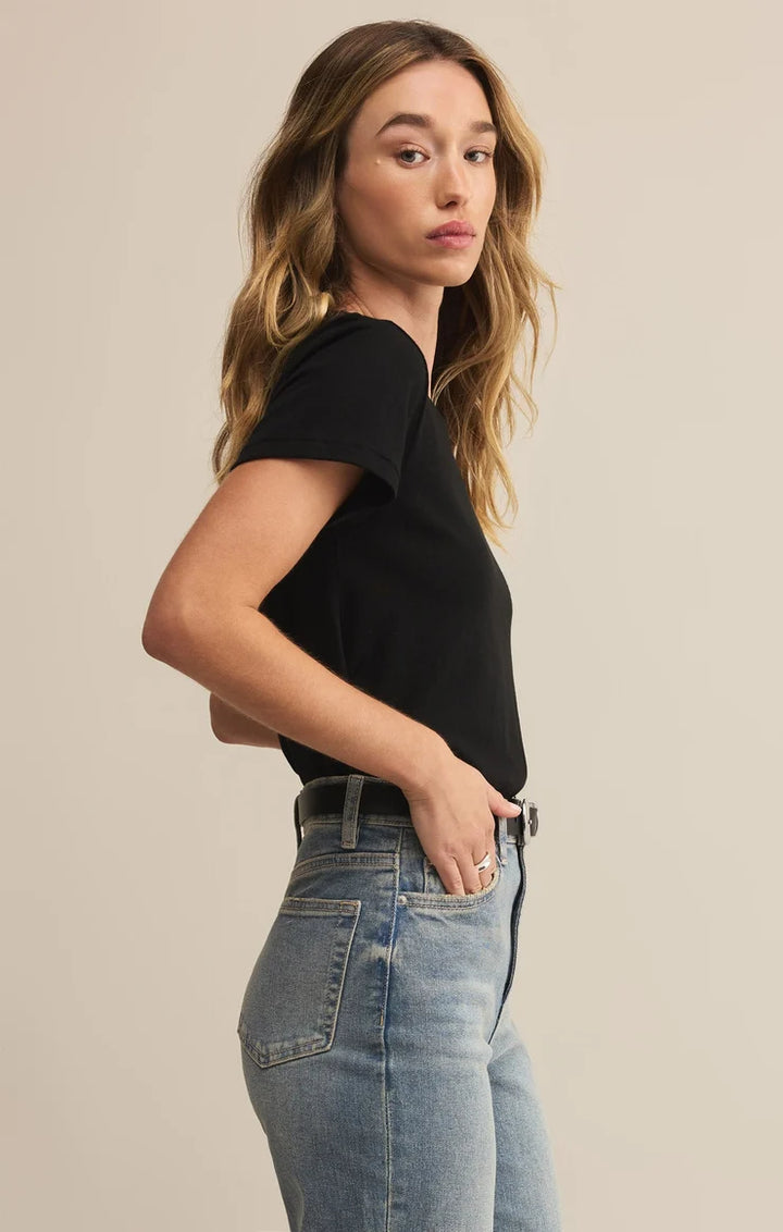 Woman wearing a black t-shirt and blue jeans against a beige background